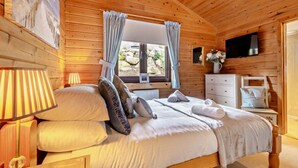 Ein Schlafzimmer einer Holzhütte mit einem Bett, Vorhängen, einem Fernseher und einer Kommode.