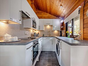A compact kitchen with white cabinets, a microwave, a sink, and a washing machine.