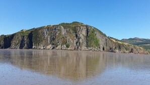 Eine Küstenlandschaft mit einem großen Hügel und ruhigem Gewässer, das den Hügel widerspiegelt.