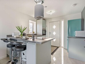 A modern kitchen with a central island, bar stools, a built-in oven, and a refrigerator. - 1 Bed in Bude (oc-93958) (Jacobstow)