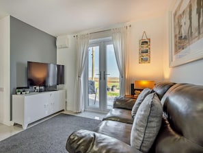 Ein Wohnzimmer mit einer Ledersofa, einem Flachbildfernseher, einer weißen Kommode und einer Tür zu einem Außenbereich.