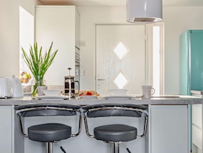 Eine moderne Küche mit einer zentralen Kochinsel, zwei Barhocker, einer Kaffeemaschine und einem Kühlschrank.