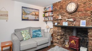 A cozy living room with a grey sofa, a stone fireplace, a bookshelf, and a framed picture of the Great Western Railway. - 2 Bed in Brixham (oc-93990) (Brixham)