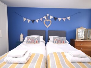 A bedroom with two beds, a blue wall, a heart-shaped decoration, and a string of triangular flags. - 2 Bed in Brixham (oc-93990) (Brixham)