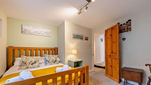 A bedroom with a wooden bed, a bedside table with a lamp, a small wooden cabinet, and a chair. - 2 Bed in Brixham (oc-93990) (Brixham)