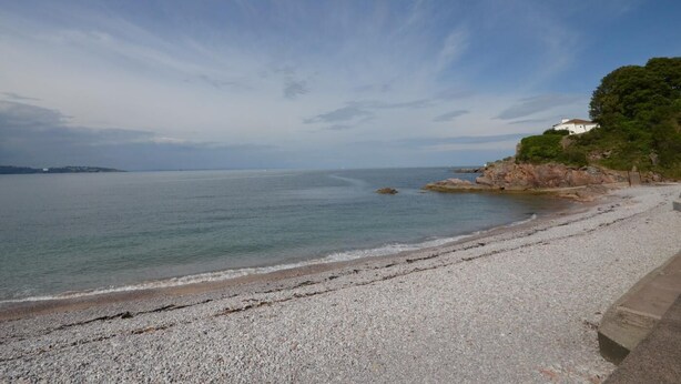 A pebble beach with a clear view of the sea and a white building on a hill. - 2 Bed in Brixham (oc-93990) (Brixham)