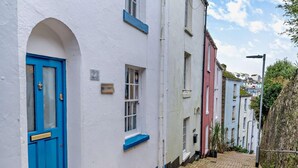 A narrow street with white buildings, a blue door, and a small window. - 2 Bed in Brixham (oc-93990) (Brixham)