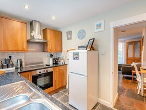 A modern kitchen with wooden cabinets, a stainless steel range hood, a white refrigerator, and a built-in oven. - 2 Bed in Brixham (oc-93990) (Brixham)