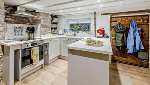 A modern kitchen with white cabinetry, a central island, a stone accent wall, and a wooden door with coats hanging.