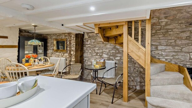 A rustic interior with a stone wall, wooden staircase, and a dining area with chairs and a table.