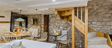 Un intérieur rustique avec un mur en pierre, un escalier en bois et un coin repas comprenant des chaises et une table.