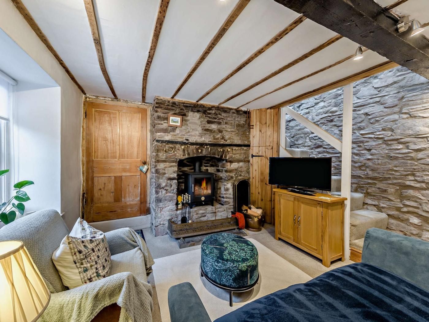 A cozy living room with a stone fireplace, wooden beams, a television, and comfortable seating.