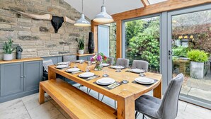 A dining area with a wooden table, grey chairs, and a bench. There is a stone wall with a mounted animal head and potted plants. - 6 Bed in Huddersfield (oc-93984) (Huddersfield)
