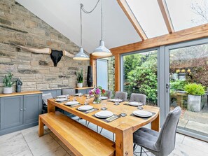 A dining area with a wooden table, grey chairs, and a bench. There is a stone wall with a mounted animal head and potted plants. - 6 Bed in Huddersfield (oc-93984) (Huddersfield)