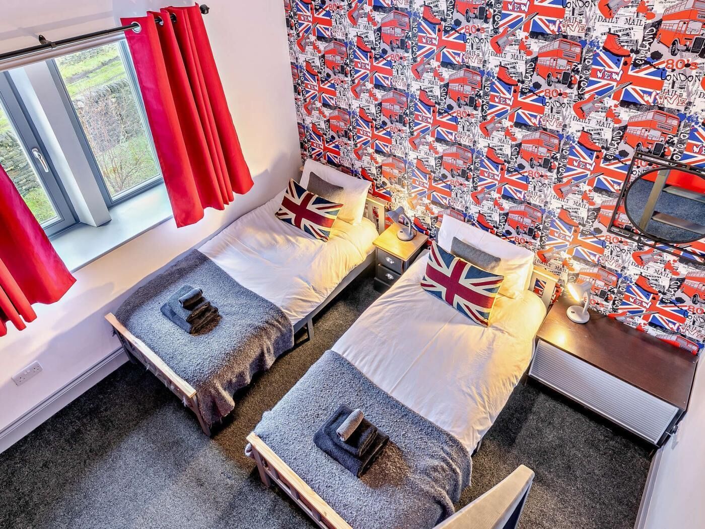 Una habitación con dos camas, una ventana con cortinas rojas y una pared decorada con motivos británicos.