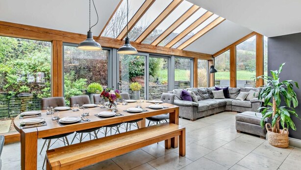 A spacious room with a large dining table, a sofa, and a bench. There are large windows and a skylight. - 6 Bed in Huddersfield (oc-93984) (Huddersfield)