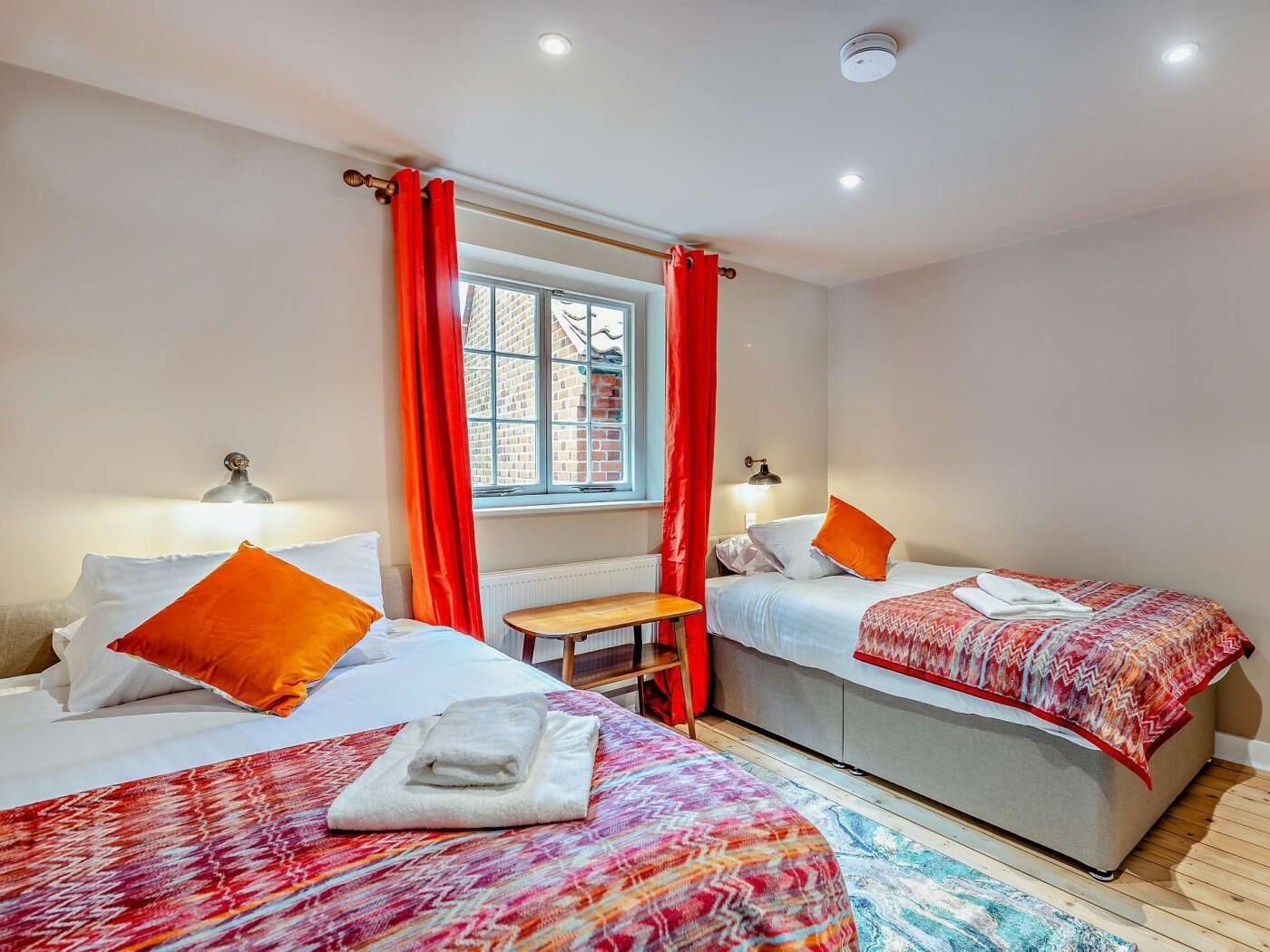 Une chambre avec deux lits, des rideaux rouges, une fenêtre et une petite table.