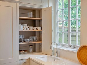 A kitchen with open cabinets, a sink, and a window with a view of greenery.
