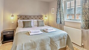 A bedroom with a bed, bedside lamps, a nightstand, a window with curtains, and a radiator.