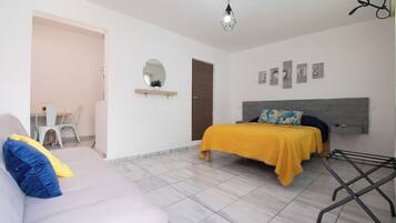 A bedroom with a bed, a sofa, a chair, a mirror, and a hanging light fixture.