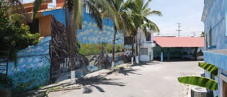 A street with buildings, palm trees, and a mural.