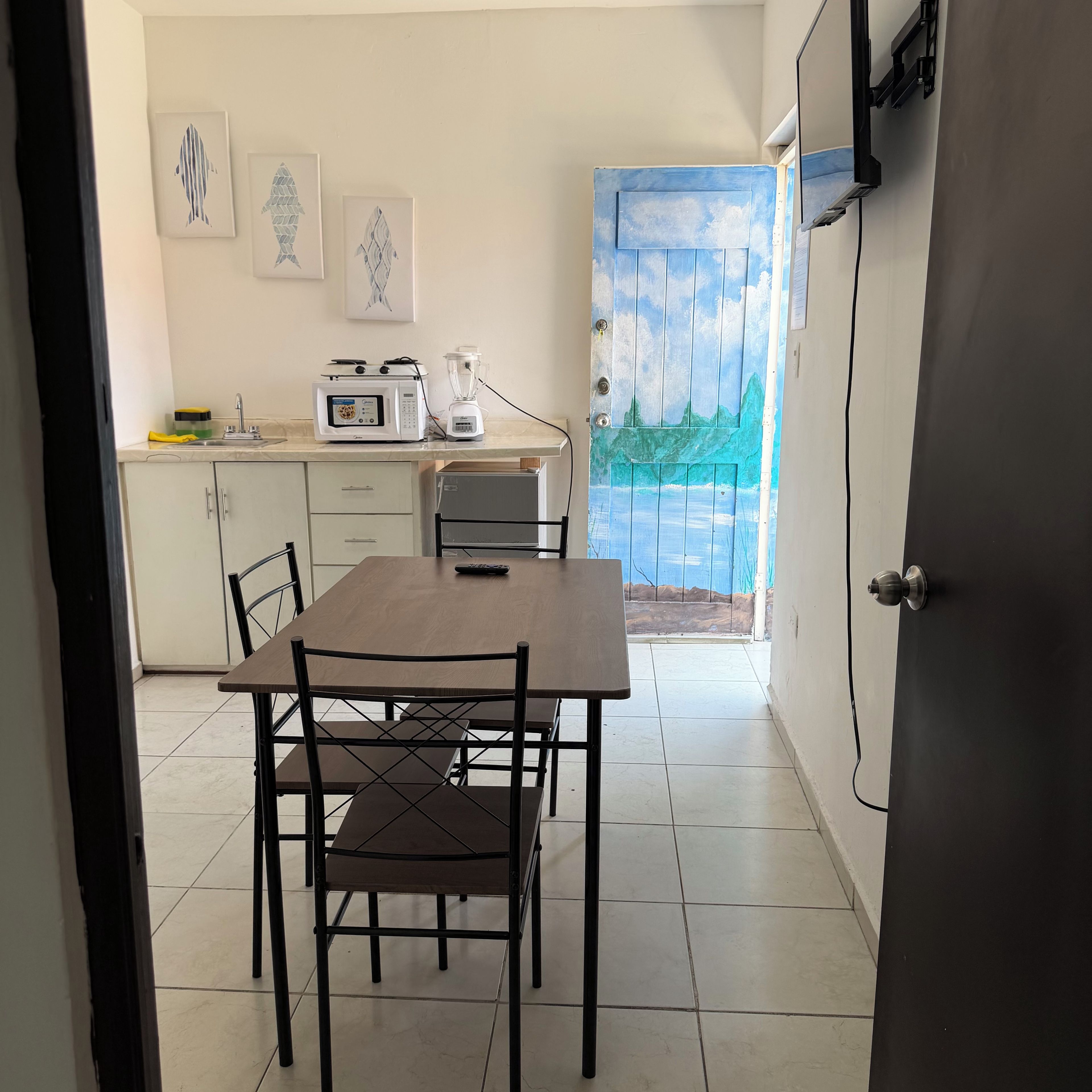 Un comedor con mesa y sillas, una cocina con electrodomésticos, y una puerta que da a un balcón.