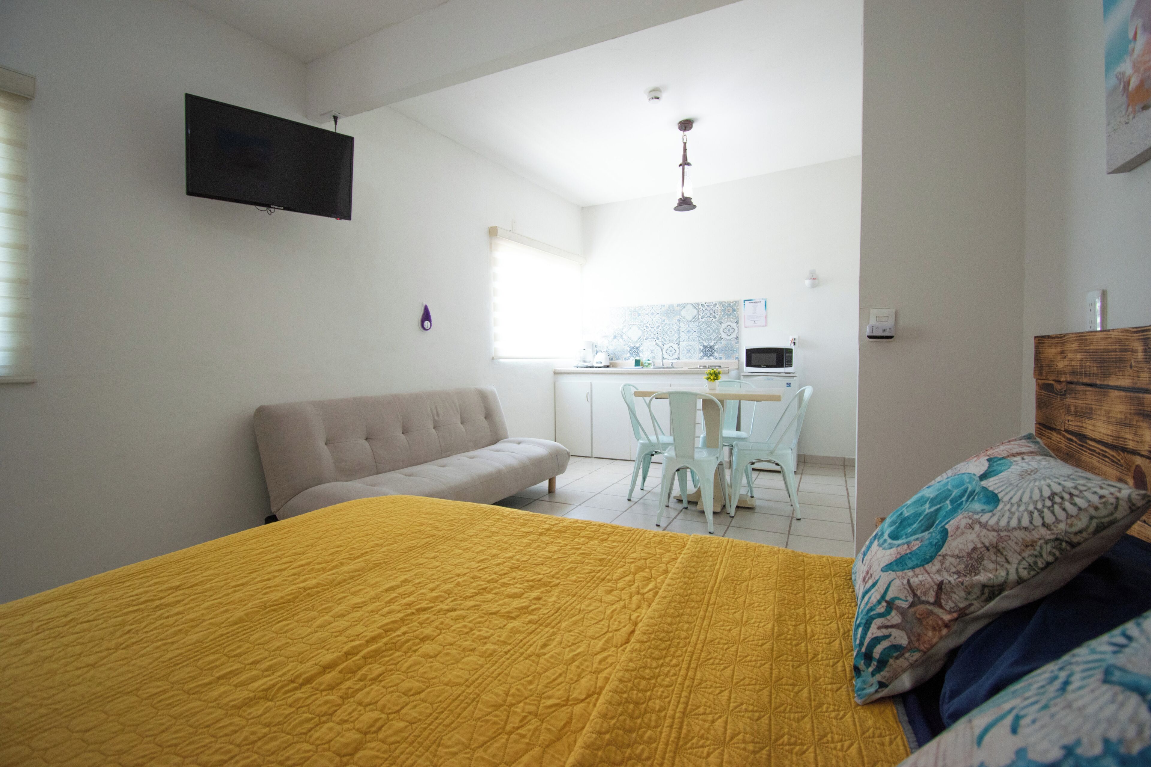 Un dormitorio con cama, sofá, televisor, zona de comedor con mesa y sillas, y área de cocina con microondas.