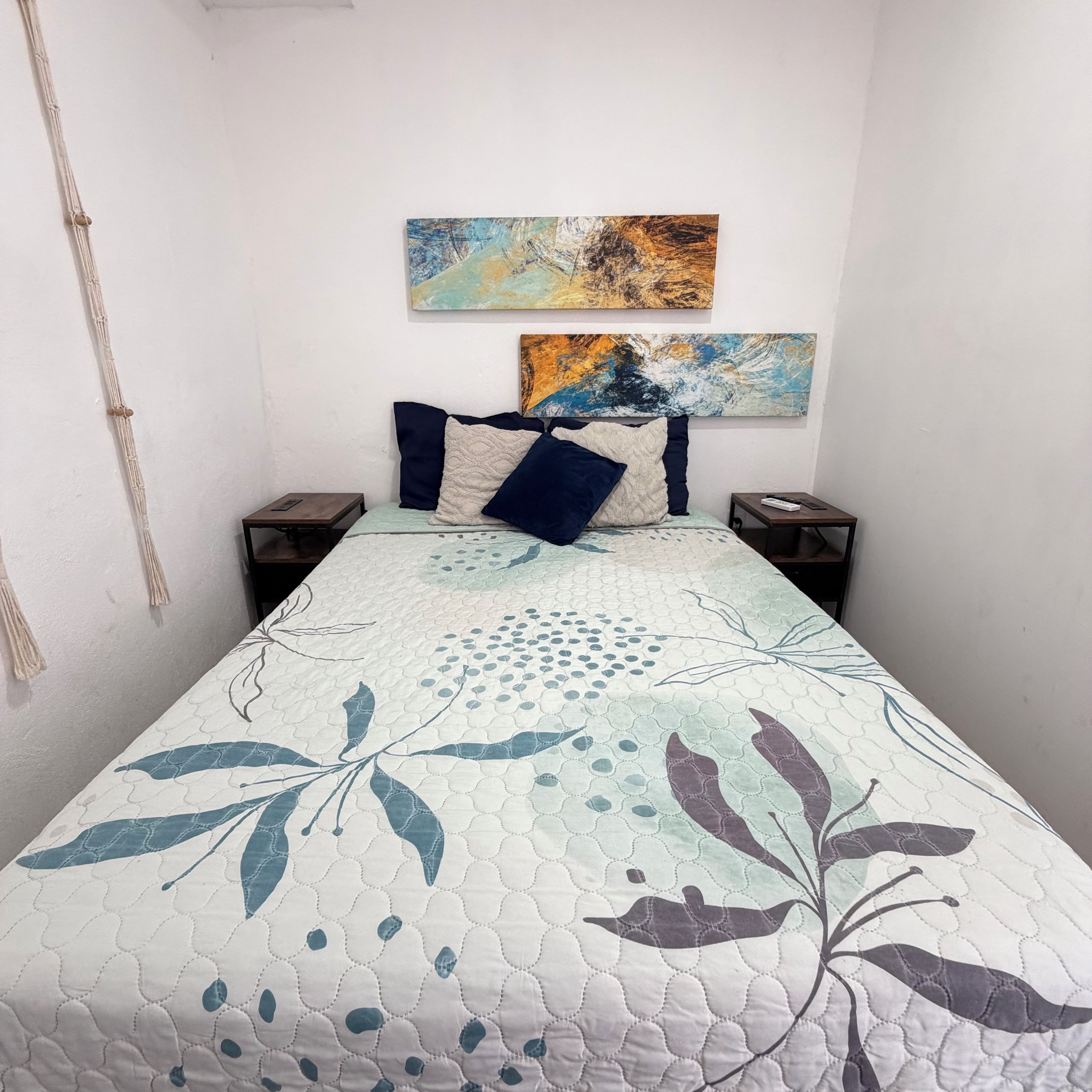 A bed with a quilted headboard, two bedside tables, and a wall-mounted abstract painting.