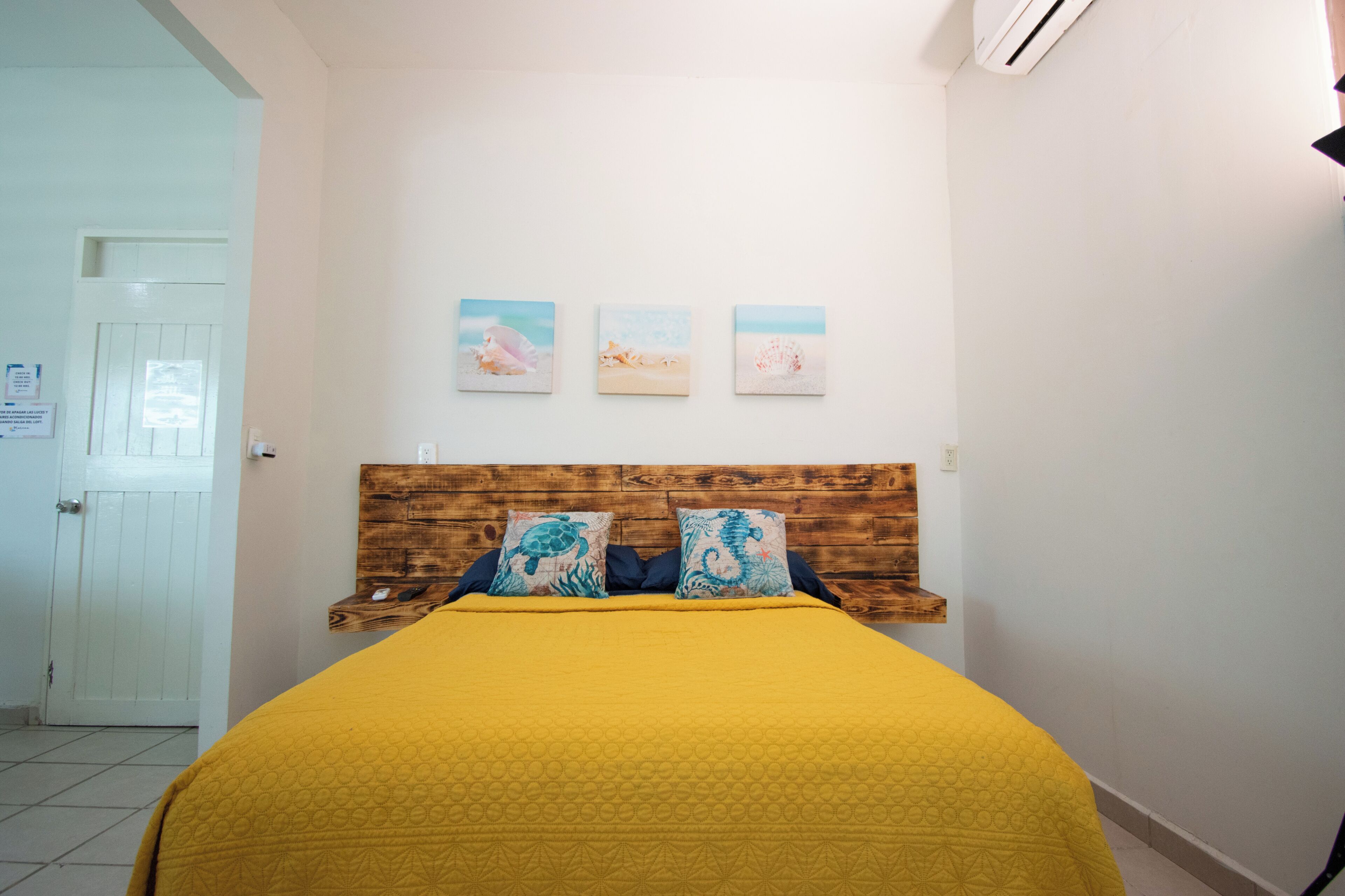 Une chambre à coucher avec une t ête de lit en bois, une couvre-lit jaune et trois tableaux accrochés au mur.
