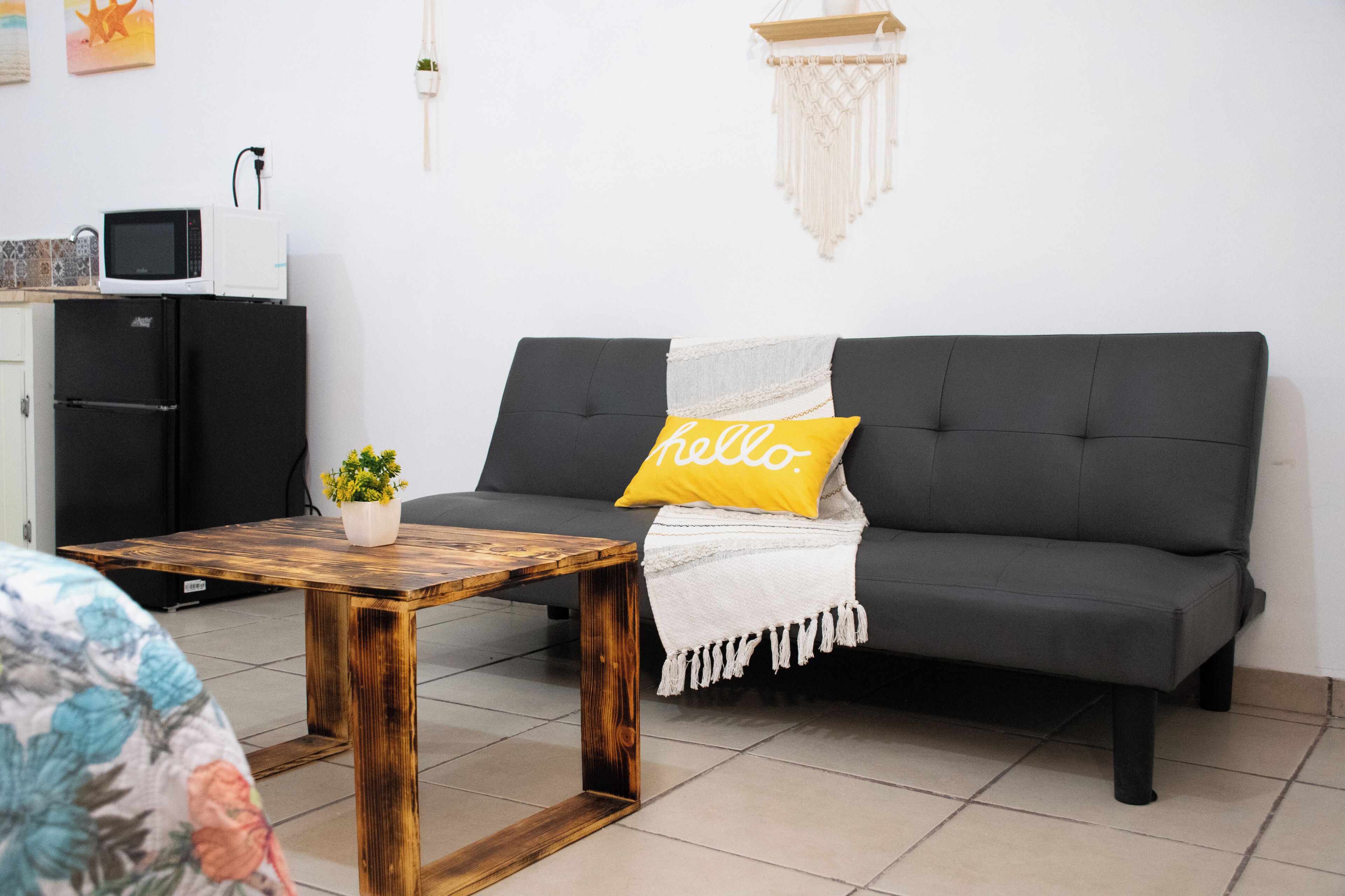 Una sala de estar moderna con un sofá gris, una mesa de centro de madera, una planta pequeña en maceta y una almohada con la palabra 'hello'.