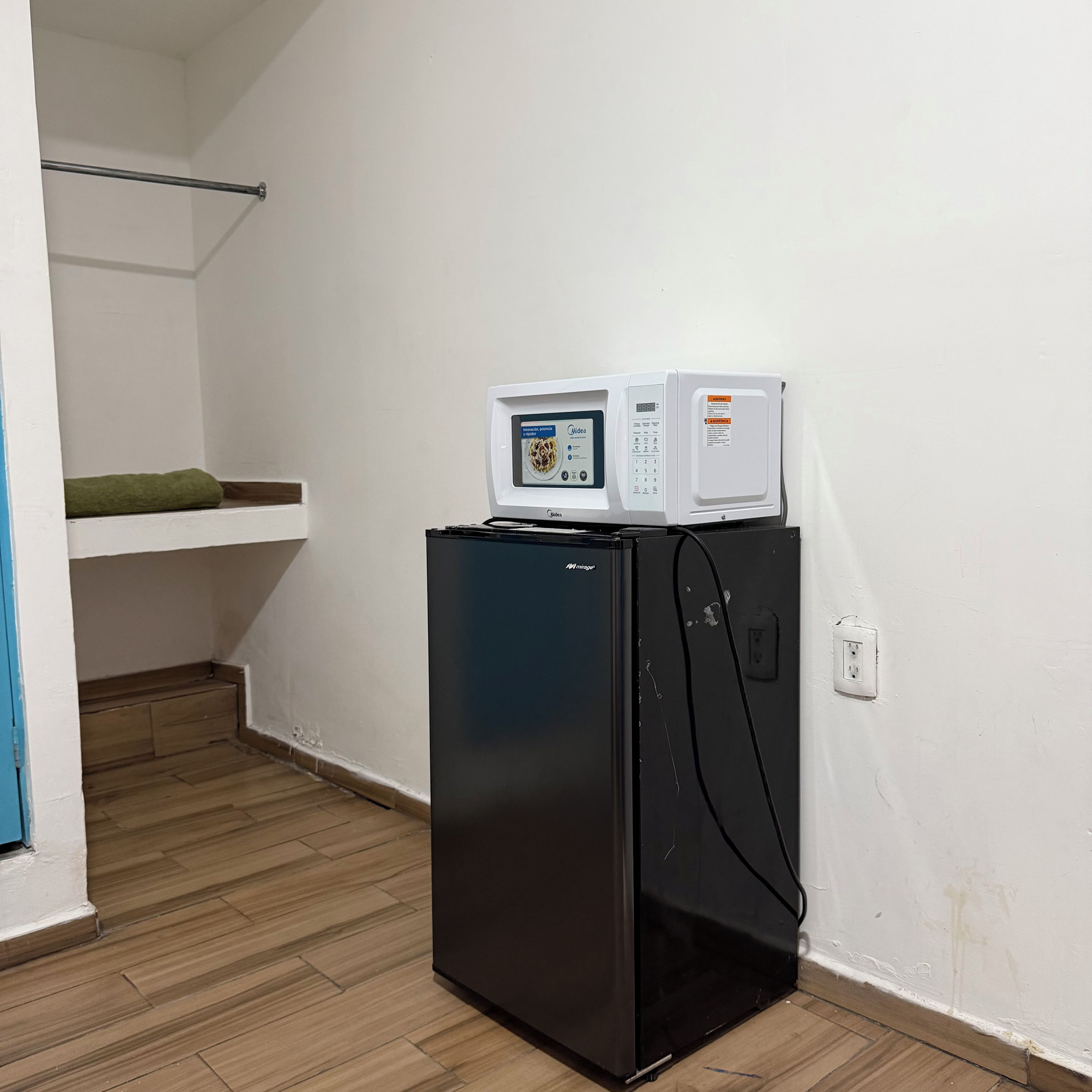 Un refrigerador negro con un microondas encima, piso de madera y pared blanca.