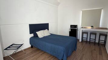 Una habitación con una cama, un escritorio con espejo, un taburete pequeño, un microondas y un equipo de aire acondicionado.