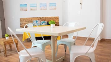 Un coin repas avec une table et quatre chaises, un lit avec une tête de lit en bois et une petite plante posée sur une table d’appoint.