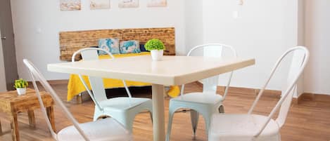 A dining area with a table and four chairs, a bed with a wooden headboard, and a small plant on a side table.