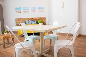 A dining area with a table and four chairs, a bed with a wooden headboard, and a small plant on a side table. - Isla Venados Renta Vacacional (Mazatlán)