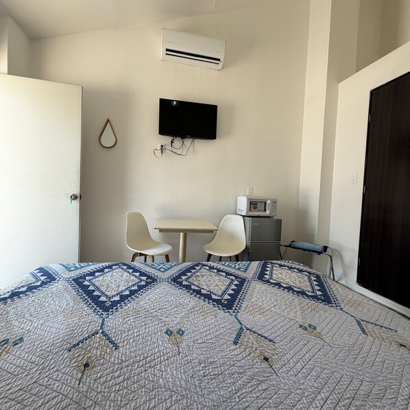 Quarto de hotel com cama, televisão, micro-ondas e duas cadeiras.