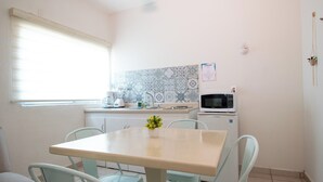 A small kitchen with a table and chairs, a microwave, and a window with blinds. - Isla Venados Renta Vacacional (Mazatlán)