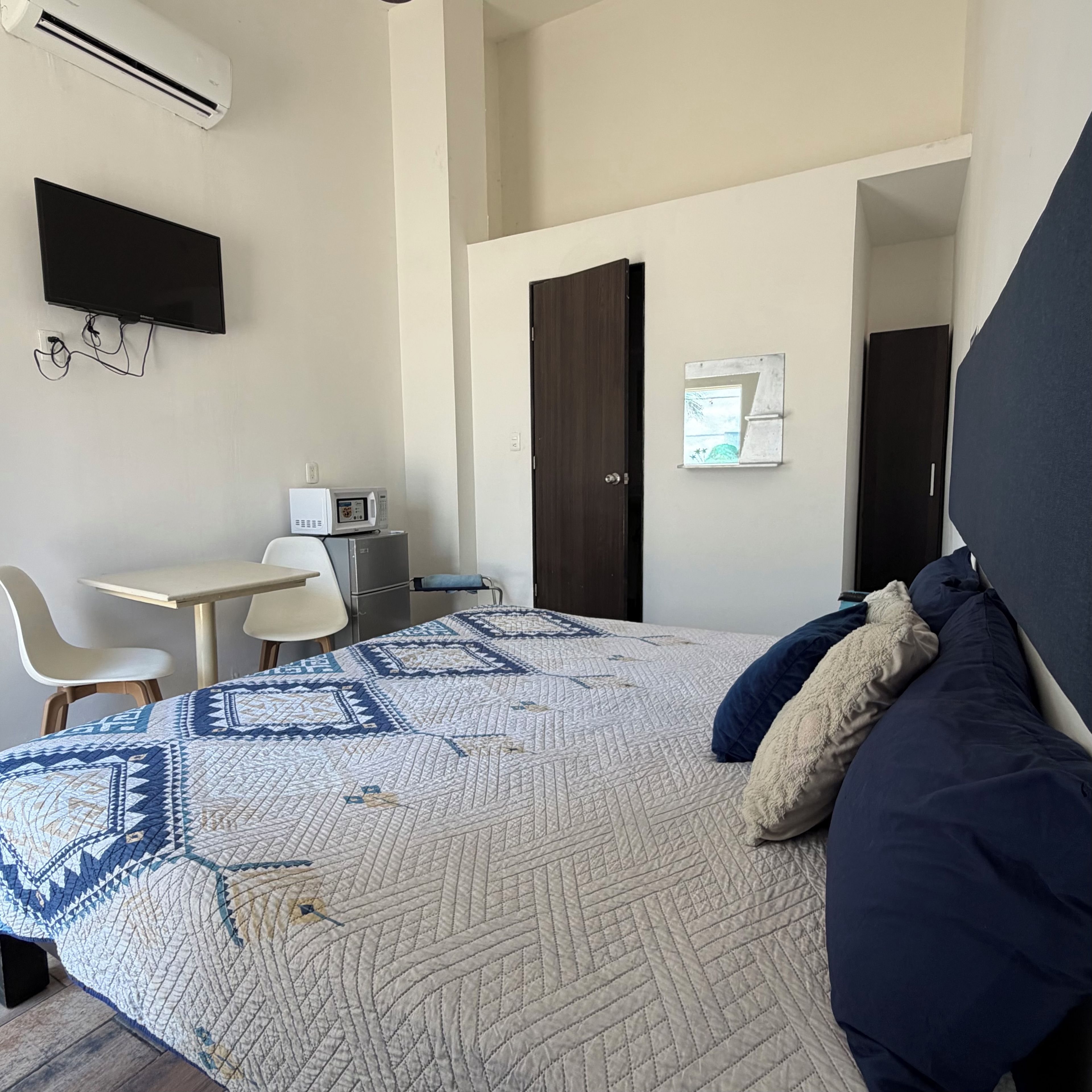 A hotel room with a bed, a desk, a chair, a flat-screen TV, and a microwave.