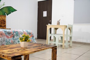 A room with a wooden table, a chair, a bed with a floral bedspread, a door, and a wall with a light switch. - Isla Venados Renta Vacacional (Mazatlán)