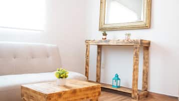 Una habitación con un sofá blanco, una mesa de madera con un jarrón de flores, una consola de madera, un espejo y una planta pequeña.