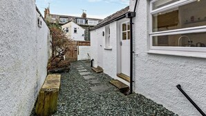 A narrow alleyway with a white building, a wooden bench, and a stone pathway. - 4 Bed in Keswick (oc-93996) (Keswick)