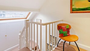 A staircase with white railings, a window with a view, and a chair with a colorful cushion. - 4 Bed in Keswick (oc-93996) (Keswick)