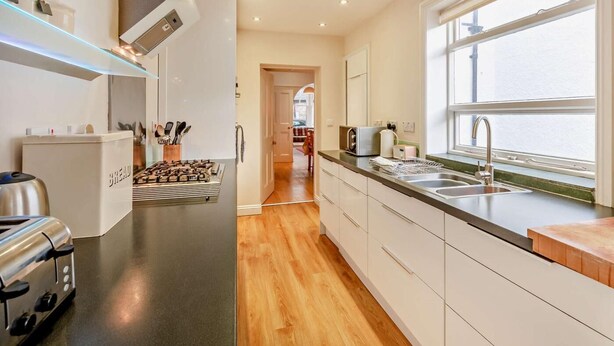 A modern kitchen with a built-in oven, a stovetop, and a window overlooking the street. - 4 Bed in Keswick (oc-93996) (Keswick)