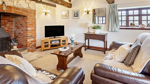 Una sala de estar con chimenea, televisor, sofás de cuero, una mesa de centro y una ventana con cortinas.