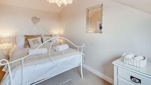 A bedroom with a white metal bed frame, a bedside lamp, a mirror, and a wicker basket on a dresser. - 3 Bed in Alnwick (oc-94013) (Alnmouth)