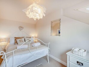 A bedroom with a white metal bed frame, a bedside lamp, a mirror, and a wicker basket on a dresser. - 3 Bed in Alnwick (oc-94013) (Alnmouth)