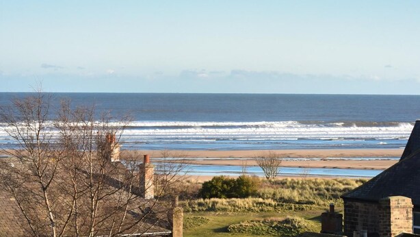 A coastal view with a beach, a stone building, and leafless trees. - 3 Bed in Alnwick (oc-94013) (Alnmouth)
