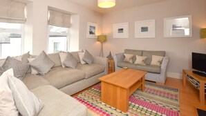 A living room with a sofa, a coffee table, a TV stand, and framed pictures on the wall. - 3 Bed in Alnwick (oc-94013) (Alnmouth)