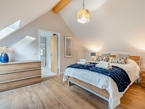 Une chambre avec un plafond en pente, un lit avec de nombreux oreillers, une lampe de chevet et un banc en bois.