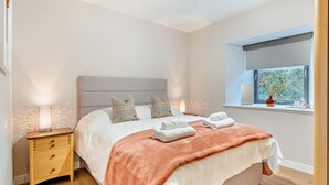 Quarto com cama, luminárias de cabeceira, mesa de cabeceira e janela com vista.